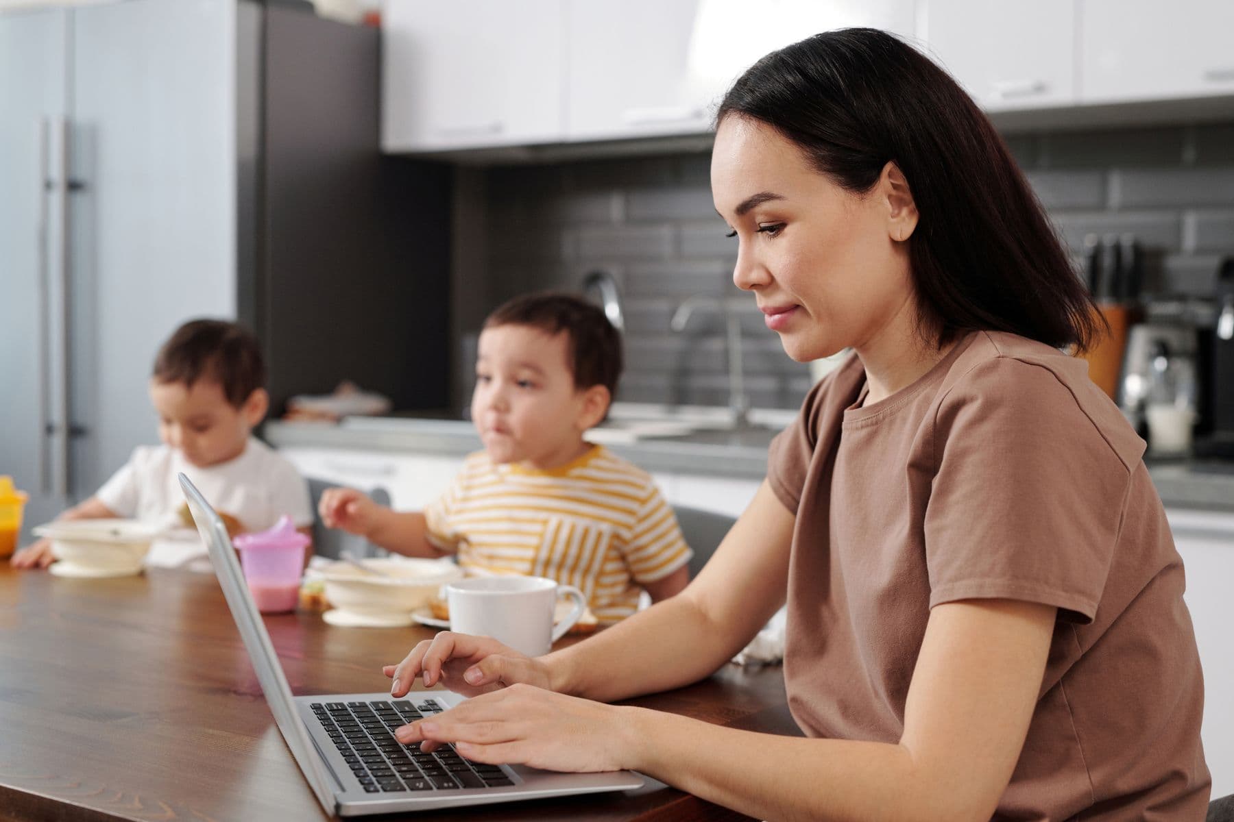 A mother working at the kitchen table while her children eat nearby
